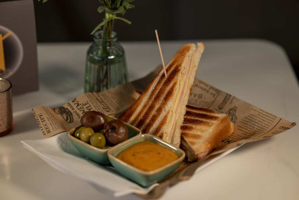 Getoastetes Sandwich mit Schinken, Käse, grünen Oliven und cremigem Dip